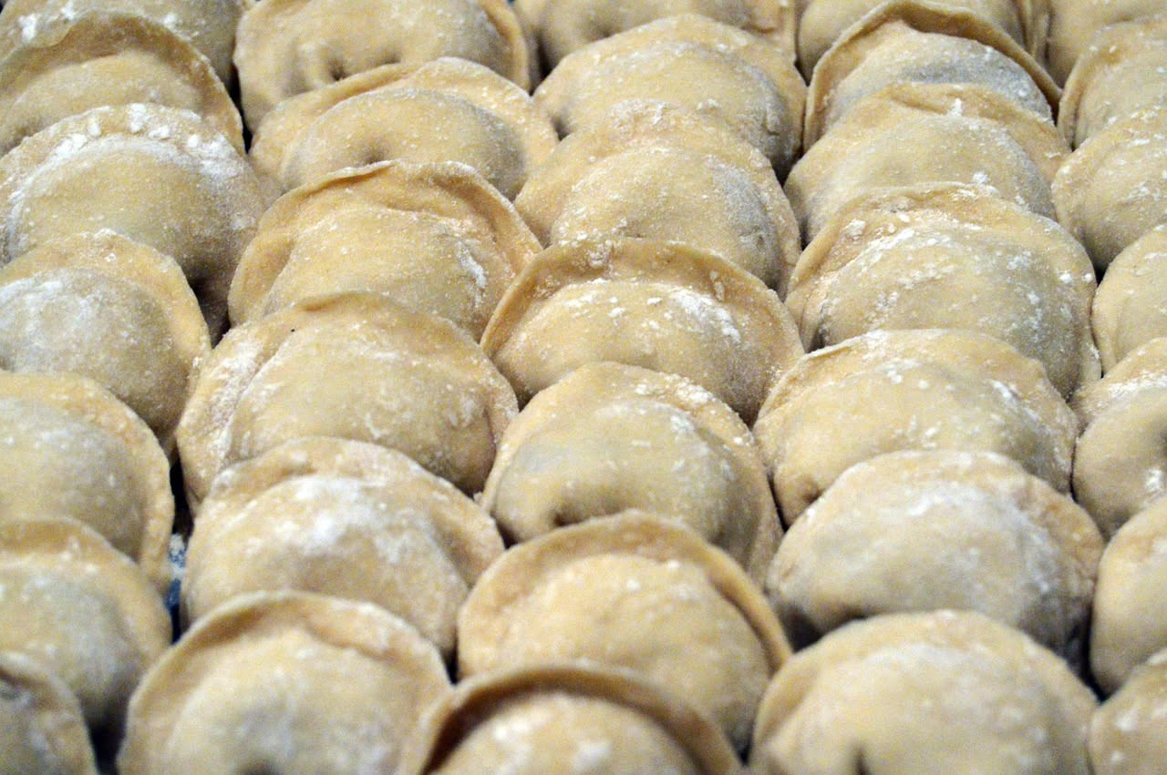 Piatto di ravioli ai funghi: pasta dorata quadrata con ripieno visibile, guarniti con prezzemolo fresco e una noce di burro dorato, su fondo di piatto bianco