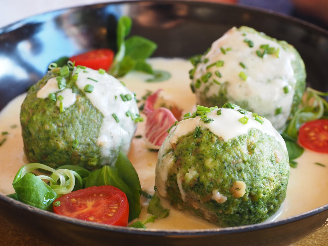 Ravioli quadrati di pasta all'uovo gialla disposti in fila su un piatto bianco, con burro fuso e salvia verde, contorno di formaggio grattugiato