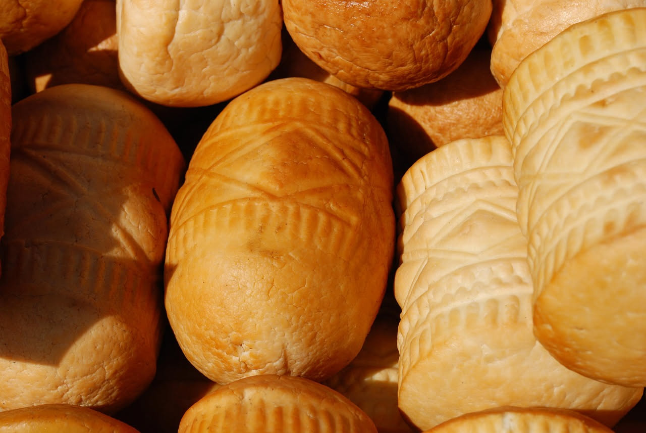 Ricotta affumicata di colore dorato-marrone con striature scure su superficie, disposta su carta alimentare, con fiamma e fumo sfocati sullo sfondo