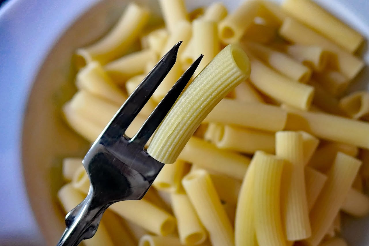 Rigatoni cremosi conditi con ragù di cipolle giallo dorato, basilico verde brillante, pinoli tostati sparsi in superficie, parmigiano grattugiato, impiattati in una ciotola bianca