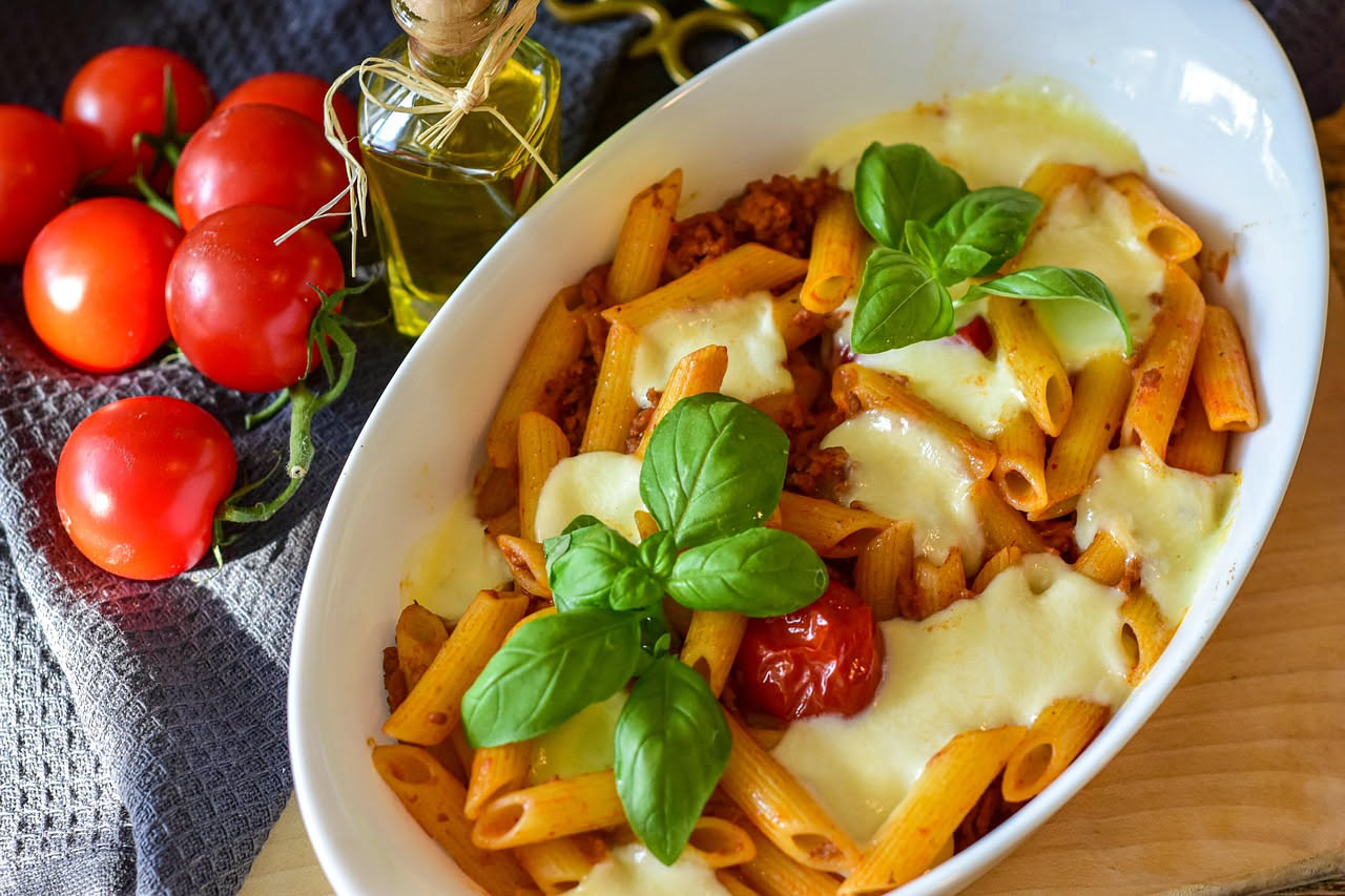 Piatto di rigatoni al dente conditi con salsa rosa cremosa, guarniti con foglia di basilico fresco e parmigiano grattugiato, presentati su piatto bianco