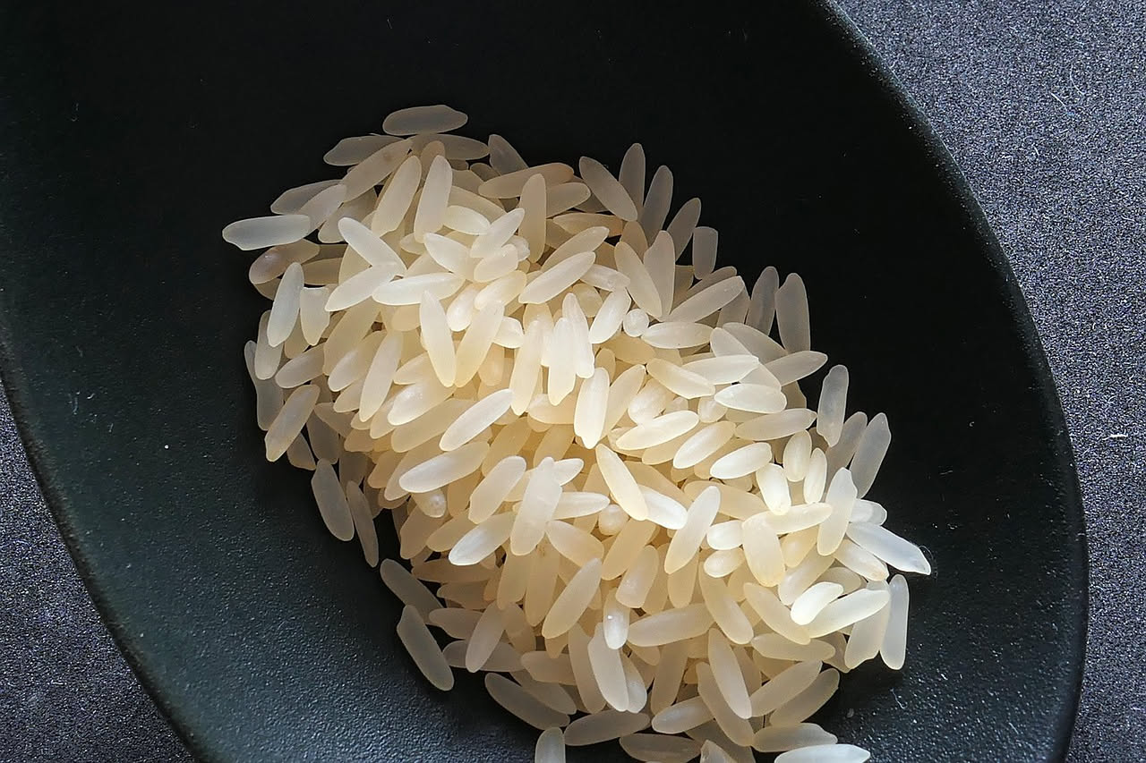 Una ciotola di ris grosso bianco crema in brodo caldo, con un mestolo che raccoglie il riso, brodo leggermente dorato, niente guarnizioni visibili, servito in una ciotola di ceramica bianca su tavolo