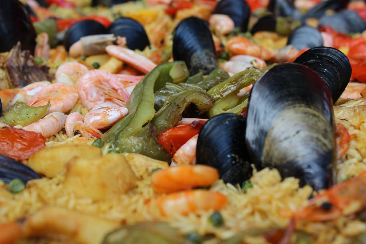 Un piatto bianco fondo con riso bianco mantecato, cozze nere aperte con la polpa visibile all'interno, gocce di sugo trasparente, prezzemolo verde su superficie, limone a spicchi sul bordo