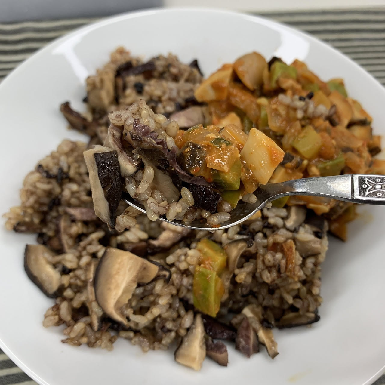 Risotto ai funghi servito in un piatto bianco, cremoso color avorio con pezzetti di funghi marroni visibili in superficie, grattugia di parmigiano e prezzemolo fresco, contorno di funghi interi sul pi