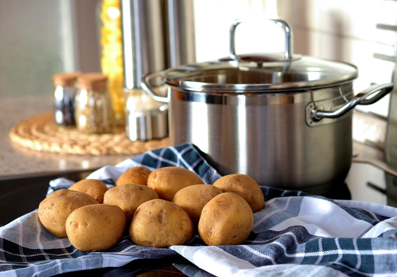 Piatto di ceramica bianca con riso e patate in brodo caldo, brodo trasparente dorato, grani di riso visibili immersi nel liquido, cubetti di patata gialla morbida, filettura di parmigiano grattugiato