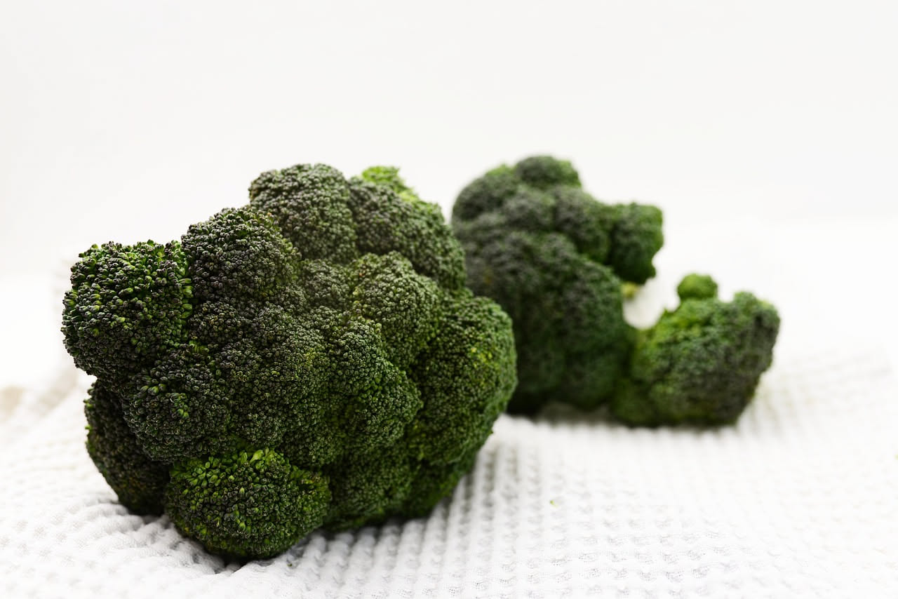 Piatto di risotto cremoso di colore verde salvia con fiorellini di broccolo fiolaro distribuiti in superficie, condito con parmigiano grattugiato e gocce di olio, servito in ciotola bianca
