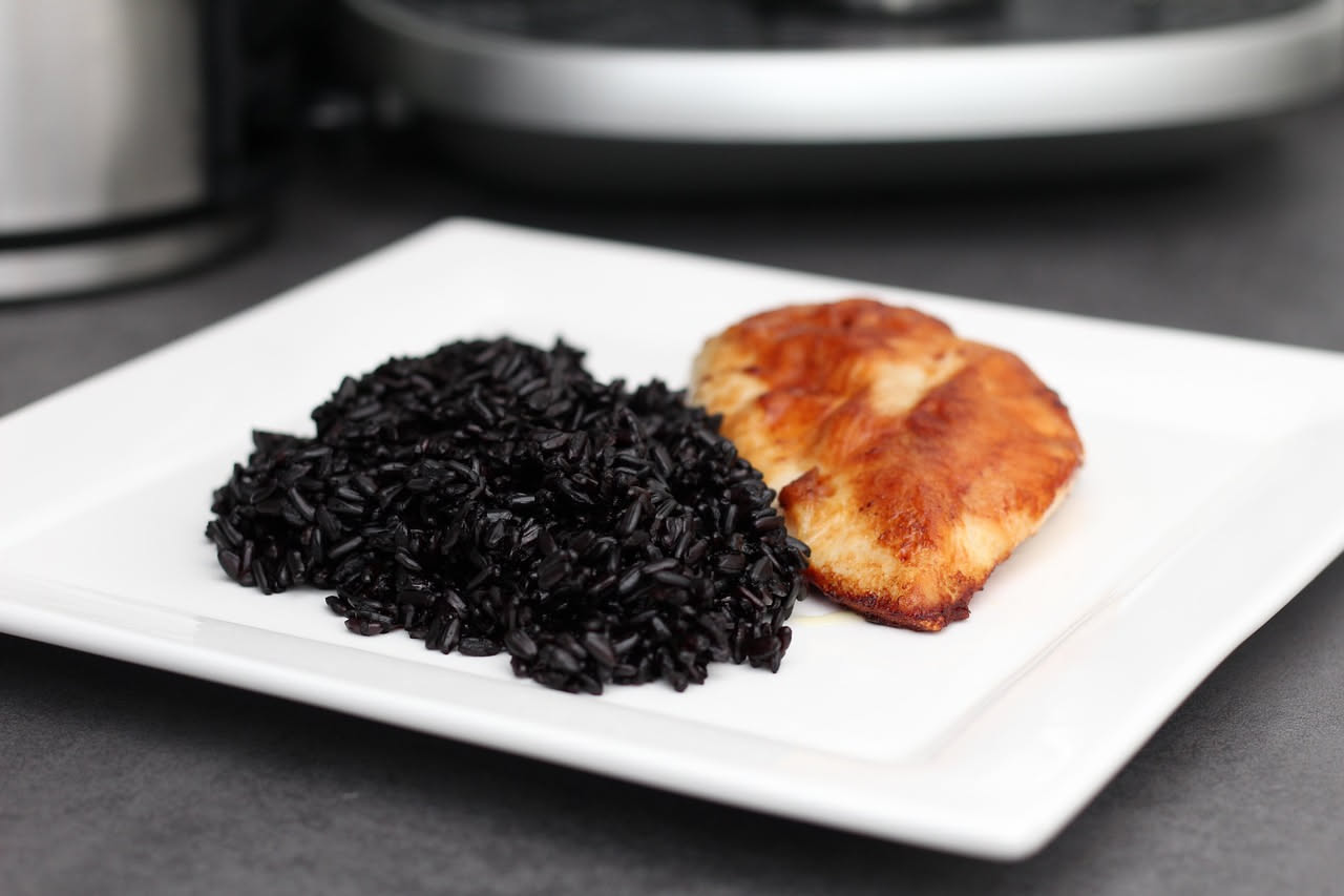 Piatto fondo bianco con risotto cremoso dal colore nero intenso, pezzi di seppia tenera sparsi uniformemente, guarnito con una fogliolina di prezzemolo fresco verde e filo di olio di oliva al centro