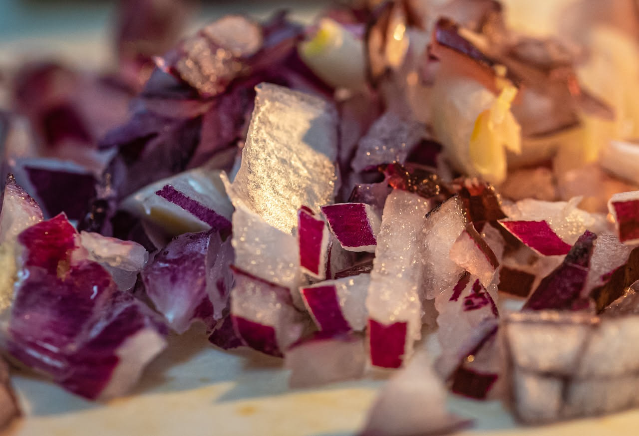 Risotto al radicchio rosso servito in piatto bianco, cremoso e dal colore viola-bordeaux intenso, guarnito con scaglie di parmigiano e un filo d'olio d'oliva, con radicchio rosso fresco sullo sfondo