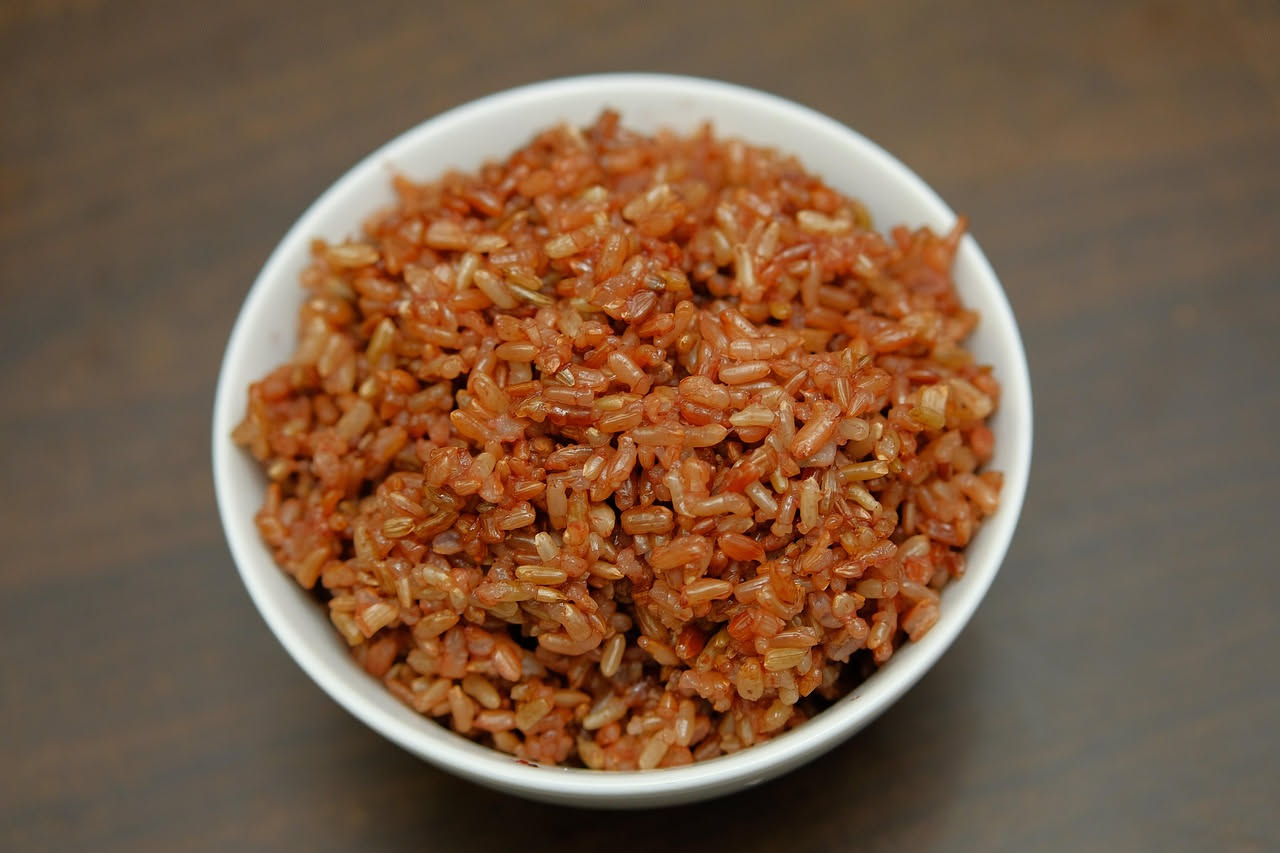 Piatto di risotto al vino rosso con colore rosso intenso, superficie cremosa, grattugiata di parmigiano bianco in cima, presentato in un piatto fondo bianco.