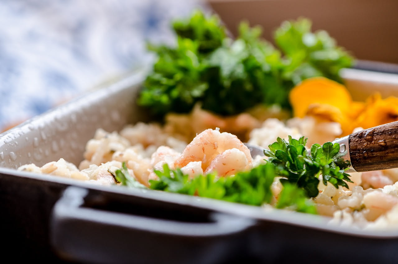Un piatto fondo con risotto all'aglione di colore beige cremoso, granelli di riso visibili e brillanti, una generosa noce di burro al centro che si scioglie, guarnito con prezzemolo verde fresco trita