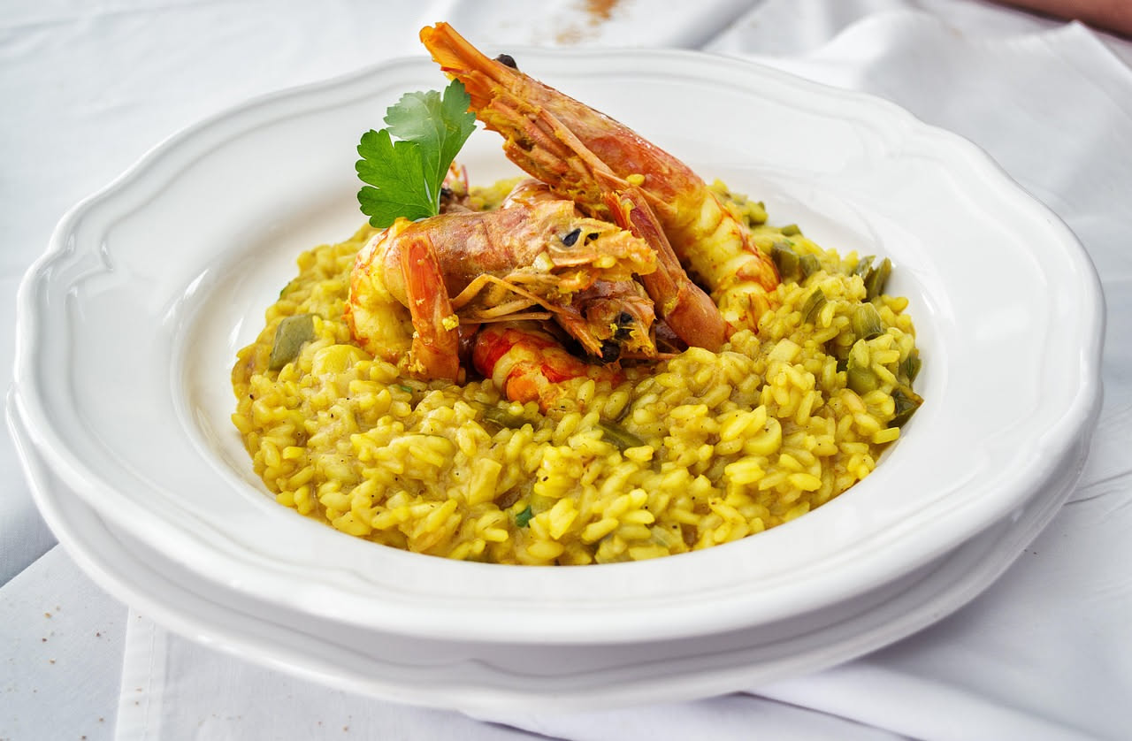 Piatto di risotto alla messinese con riso cremoso bianco, pezzi di pesce spada grigio-argento, melanzane viola scure fritte e sugo rosso di pomodoro, guarnito con prezzemolo verde e parmigiano grattug