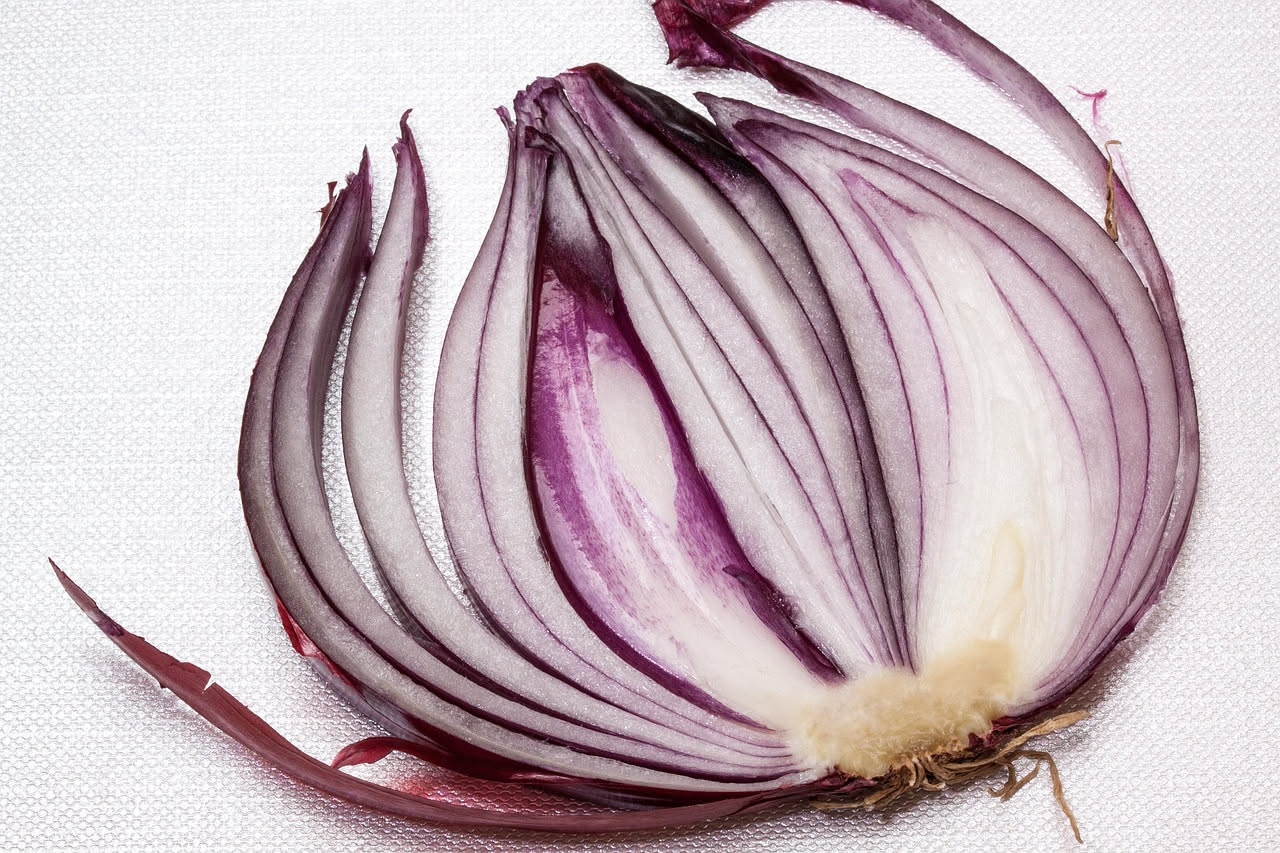 Risotto cremoso in piatto bianco con striature rosso violaceo del radicchio tritato, mantecato al centro, guarnito con una foglia di radicchio crudo e parmigiano grattugiato