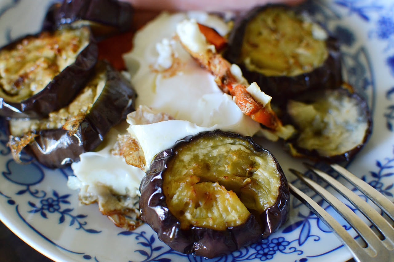 Quattro rustici di melanzane appena sfornati, dorati e croccanti, disposti su piatto bianco con melanzane grigliate visibili nel ripieno, una fogliolina di basilico sulla sommità