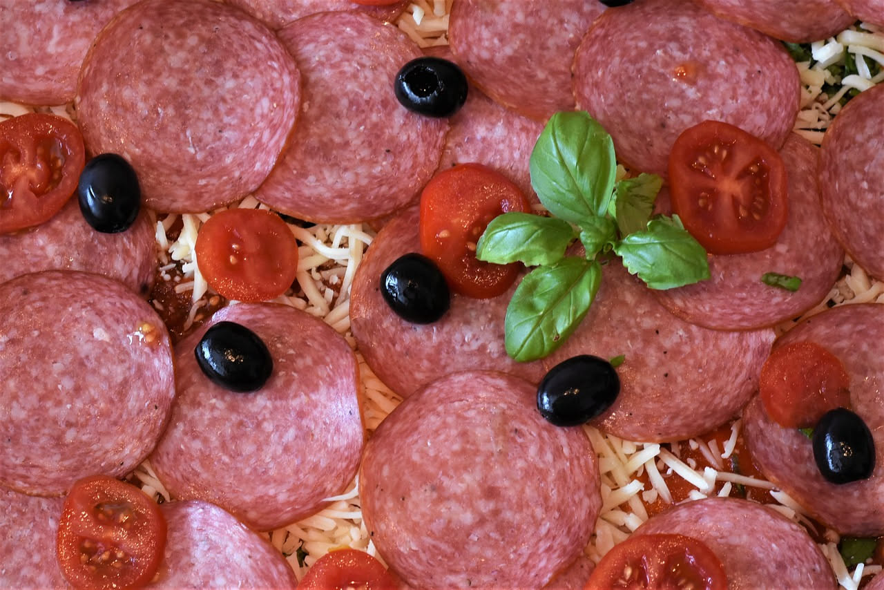 Fette di salame di Cremona dal colore rosso scuro con grasso bianco visibile, disposte su un tagliere di legno accanto a pane toscano e calice di vino rosso