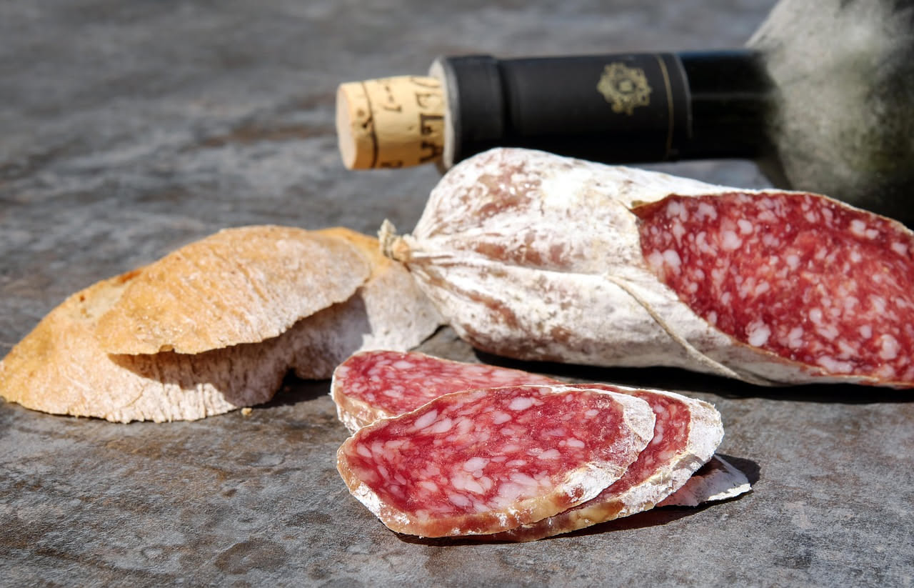 Fette di salame toscano affettato di spessore medio, con grani di pepe nero visibili sulla superficie rosa pallido, disposte su un piatto di ceramica