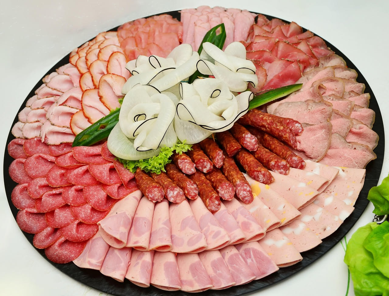 Assortimento di salami misti trentini affettati su una tavola di legno, mostrando diversi colori dal rosso scuro al rosa più chiaro, con spezie visibili nella pasta di carne