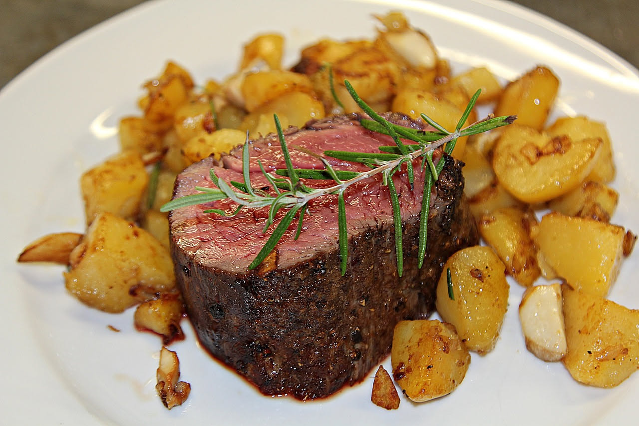 Salmì di selvaggina servito in piatto bianco fondo con carne scura e succosa, verdure brunite, salsa di vino rosso lucida, pezzi di cipolla e carota visibili, contorno di polenta bianca cremosa ai lat