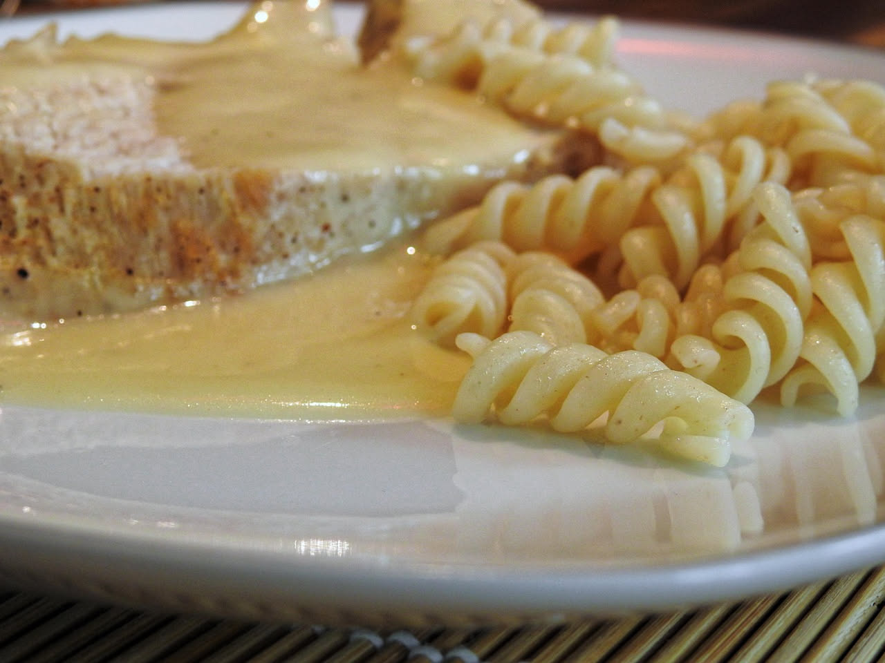 Salsa di mostarda in una ciotola bianca, color giallo ocra con semi di senape visibili, accompagnata da fette di prosciutto e formaggi su un piatto di legno chiaro