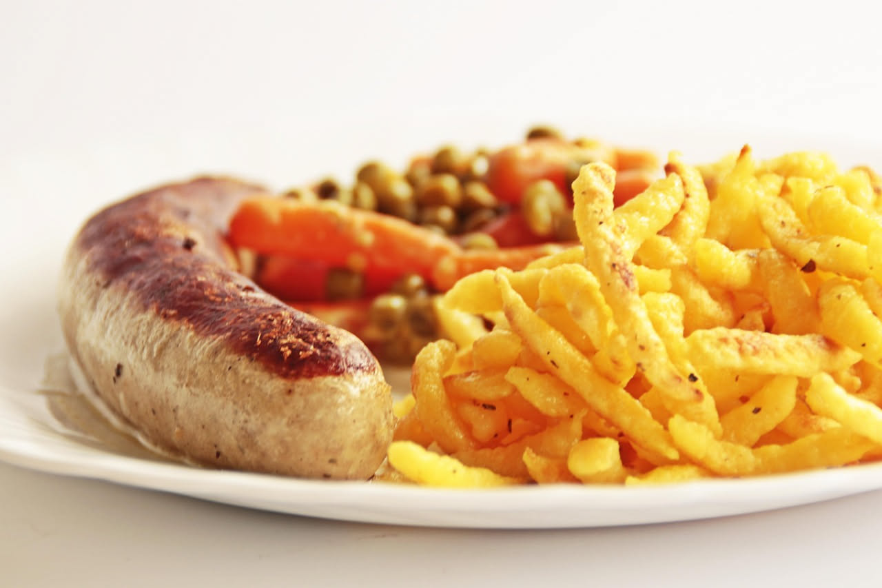 Salsiccia fritta tagliata a metà su un piatto bianco, con fuoriuscita di ripieno umido e buccia dorata croccante, accompagnata da pane tostato