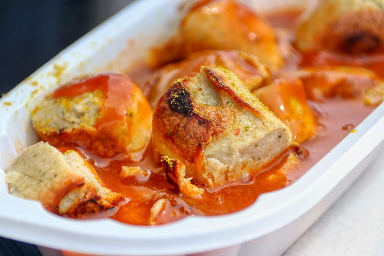 Salsiccia ripassata dorata in padella di acciaio, tagliata a metà e servita su piatto bianco con salsa brunita ai bordi