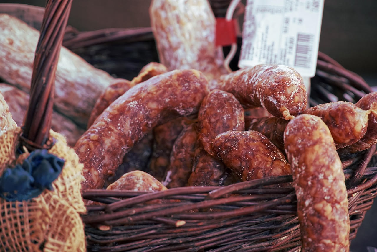 Salsicce toscane crude disposte su carta da forno con finocchietto selvatico fresco e grani di pepe nero sparsi accanto