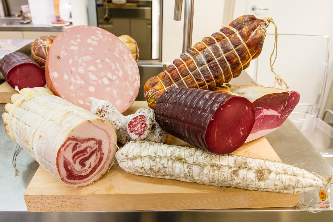 Salumi beneventani affettati su un tagliere di legno, con spezie e sale grosso sparsi attorno, in una cucina rustica con mattoni a vista