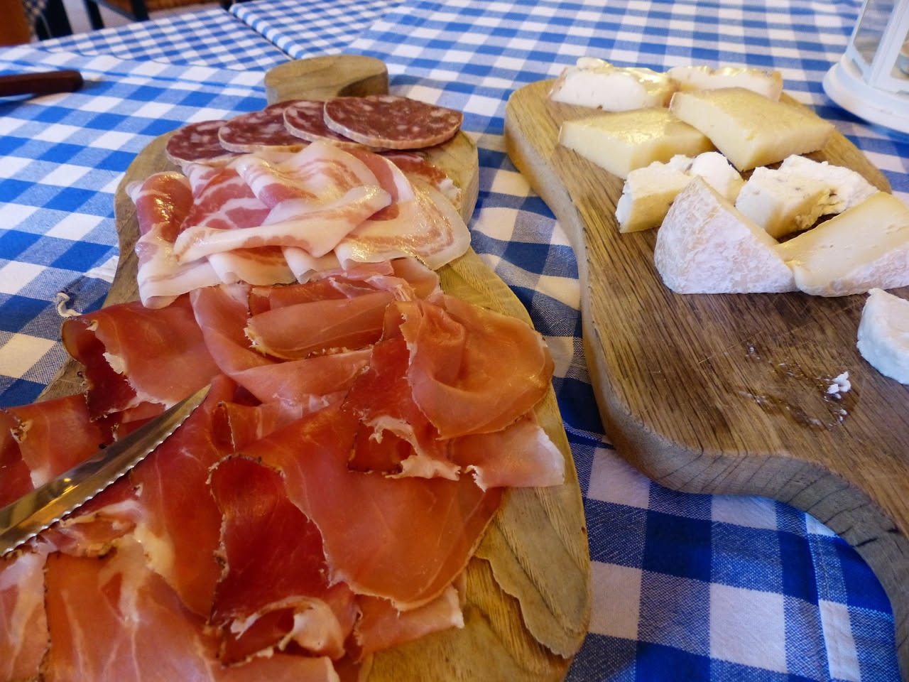 Speck di Bergamo affettato su un tagliere di legno, fette rosa striata di grasso bianco, con pezzi di pane tostato e un bicchiere di vino rosso locale accanto