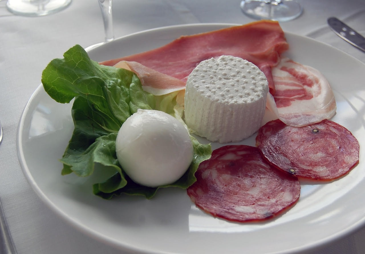 Fette di salumi toscani scuri e fragranti su un tagliere di legno con un coltello dalla lama larga, accanto un bicchiere di vino rosso