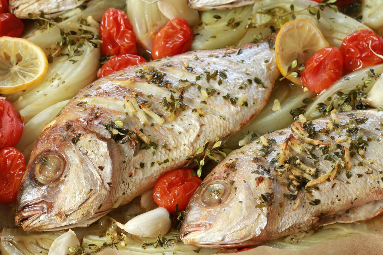 Sarago intero cotto in cartoccio di carta da forno, con fette di limone e prezzemolo fresco visibili dentro, vapore che esce dall'apertura superiore del pacco