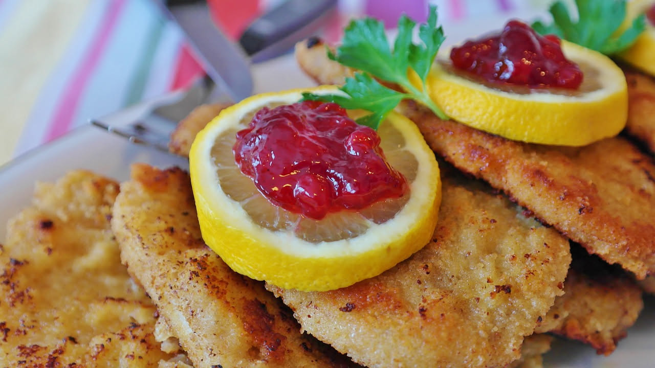 Tre scaloppine dorate e croccanti in un piatto bianco, spruzzate di limone fresco, contornate da insalata verde e limone tagliato a spicchi