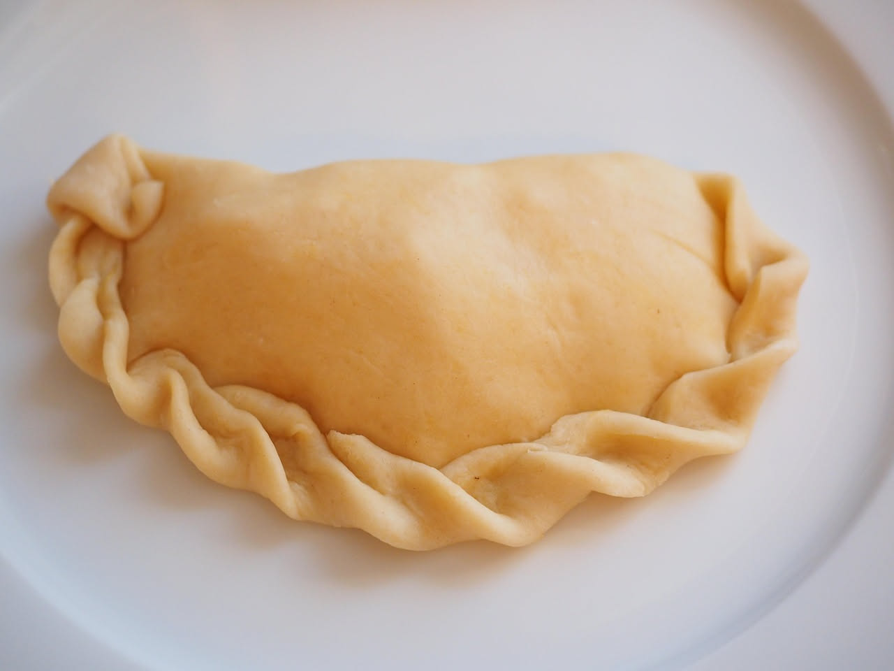Due sebadas dorate e croccanti su piatto bianco, ricoperte di miele ambrato caldo che cola sui bordi, formaggio filante visibile dal taglio, accompagnate da una ciotola di miele a lato