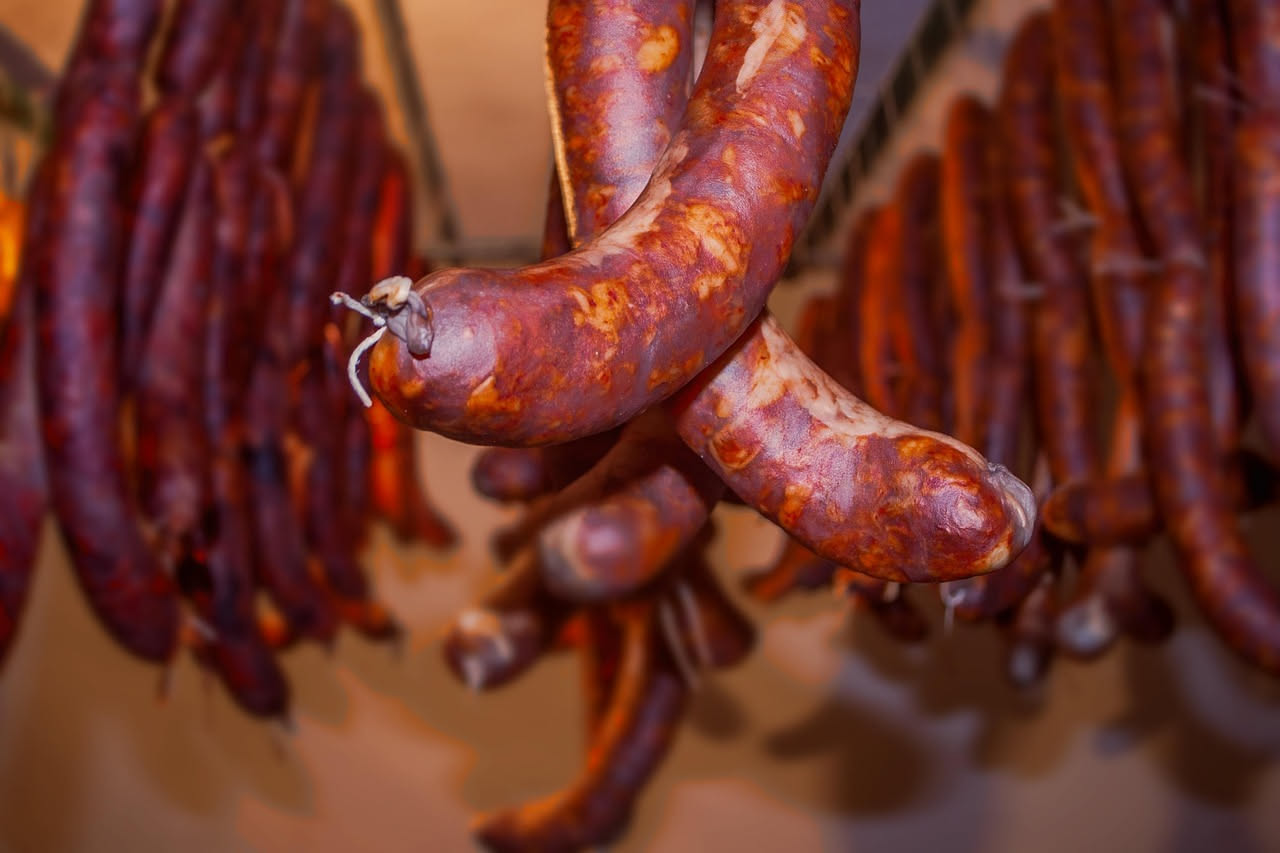 Fette di soppressata maremmana tagliate di fresco su tavolo di legno, colore rosso scuro con pepata visibile, accanto a pane toscano integrale