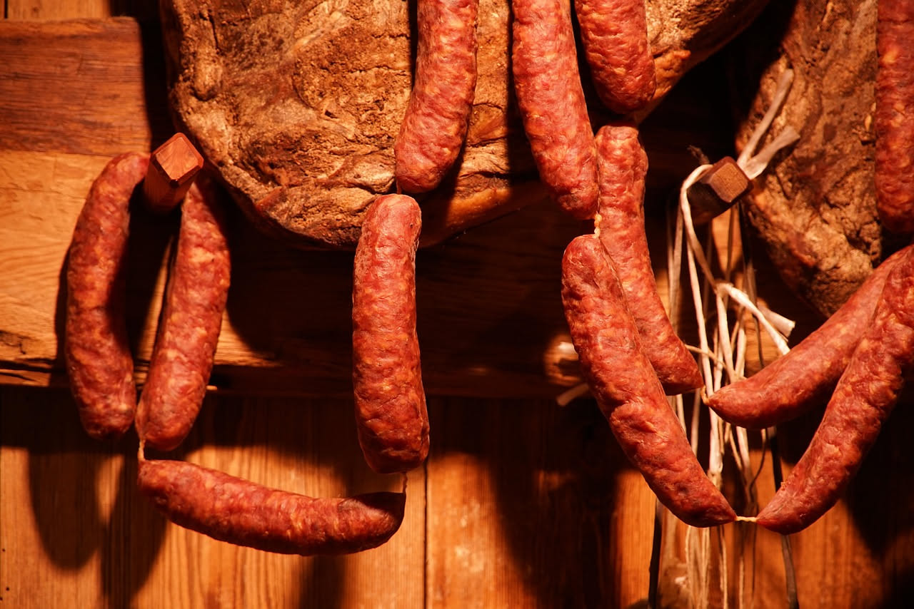 Soppressata toscana affettata su un tagliere di legno con una lama smussata, mostrando la striatura bianca del grasso e il pepe nero visibile