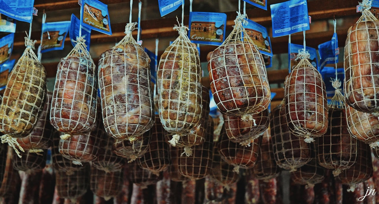 Fette di sopressata senese di colore rosso scuro con grana compatta su un tagliere di legno con spezie sparse accanto