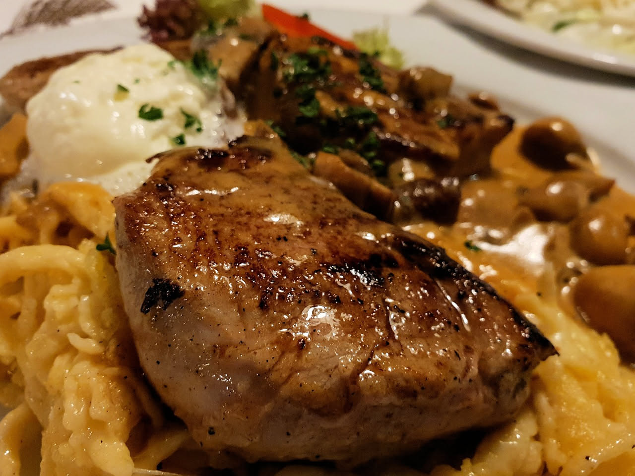 Piatto di spätzle gialli e soffici, leggermente ripassati nel burro, guarniti con prezzemolo verde fresco, serviti in una ciotola di ceramica bianca su un fondo di legno scuro