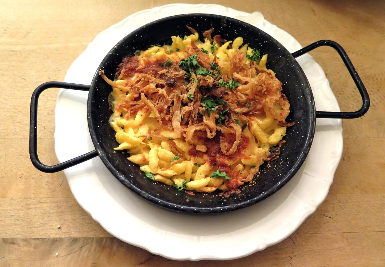 Spätzle ciociari dorati in un piatto bianco, cosparsi di parmigiano grattugiato e pepe nero, con una noce di burro fuso che scende sui lati