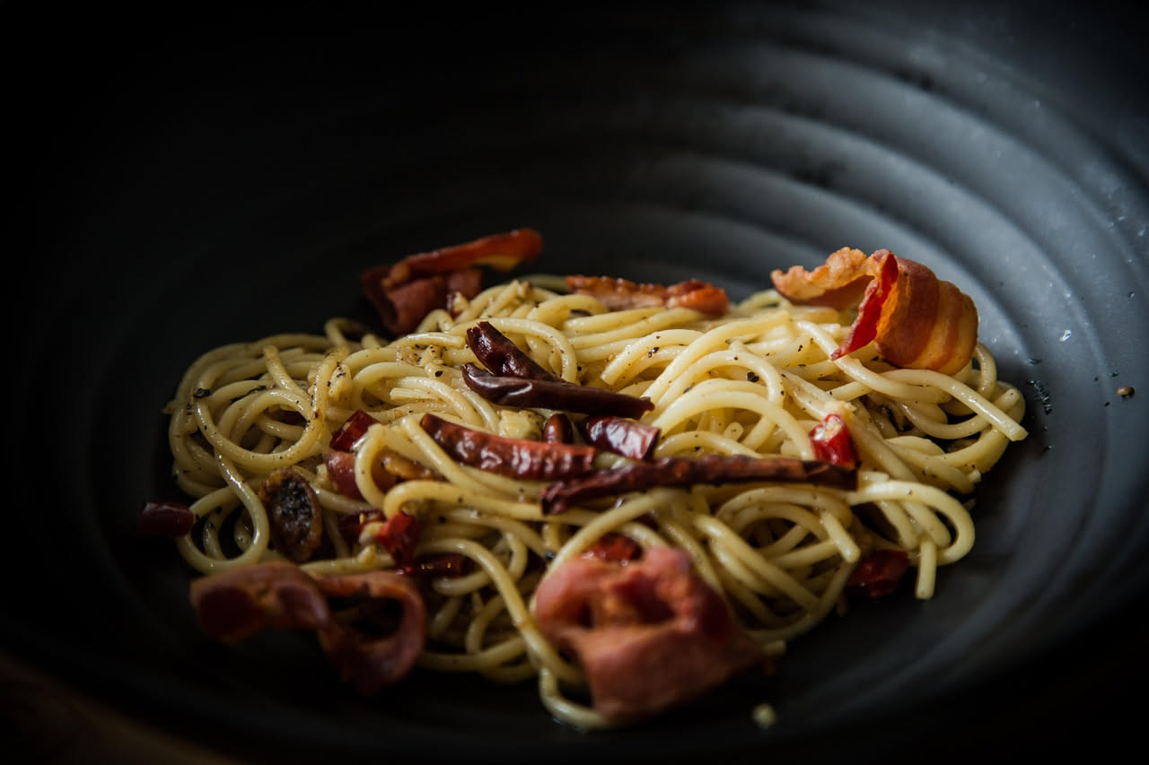 Un piatto di pasta bianca con spaghetti appena conditi, gocciole d'olio lucido tra i fili, scaglie rosse di peperoncino visibili e aglio dorato sparso uniformemente sulla superficie