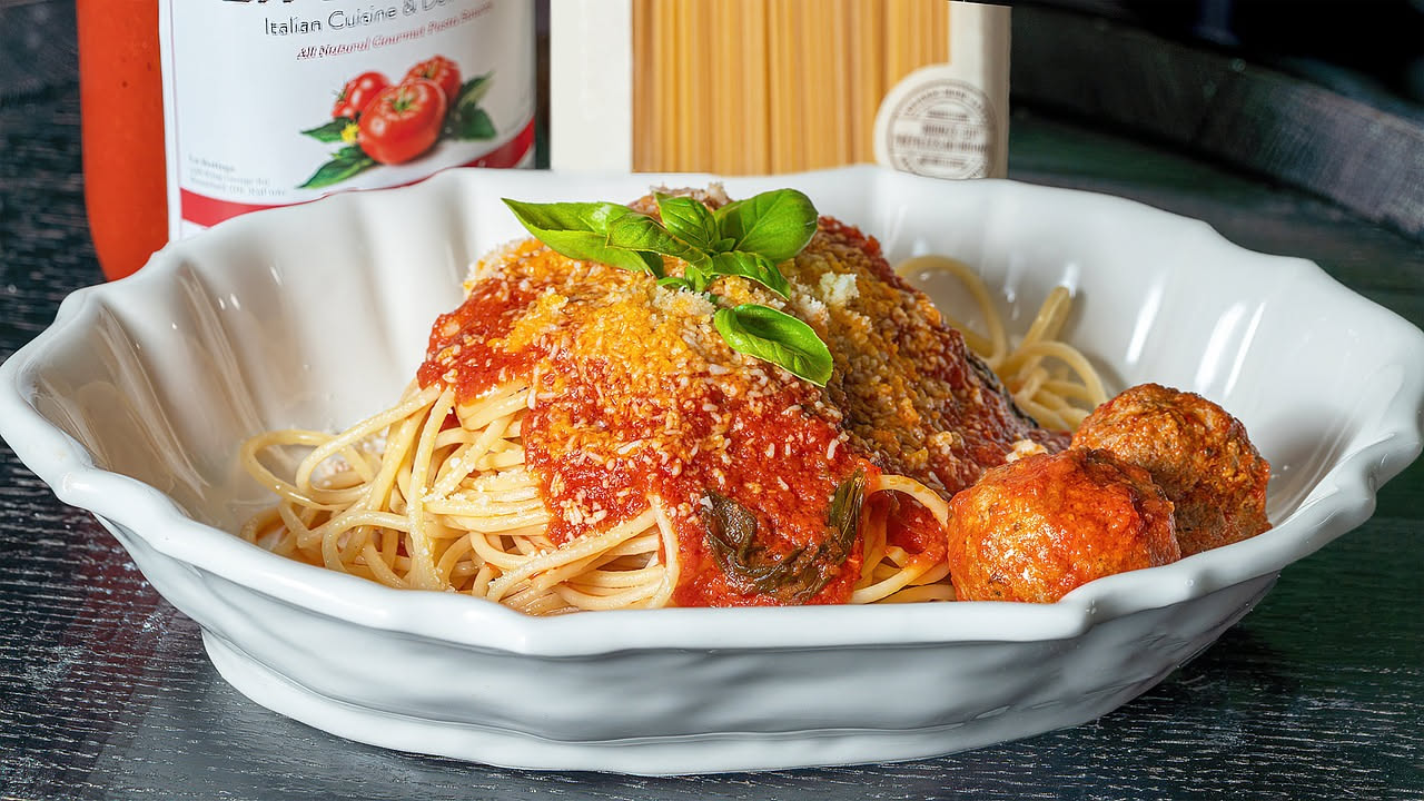 Piatto bianco con spaghetti intrecciati, ricoperti di sugo rosso brillante, gocce d'olio verde in superficie, foglia di basilico fresco verde scuro, parmigiano reggiano bianco grattugiato sparso sopra