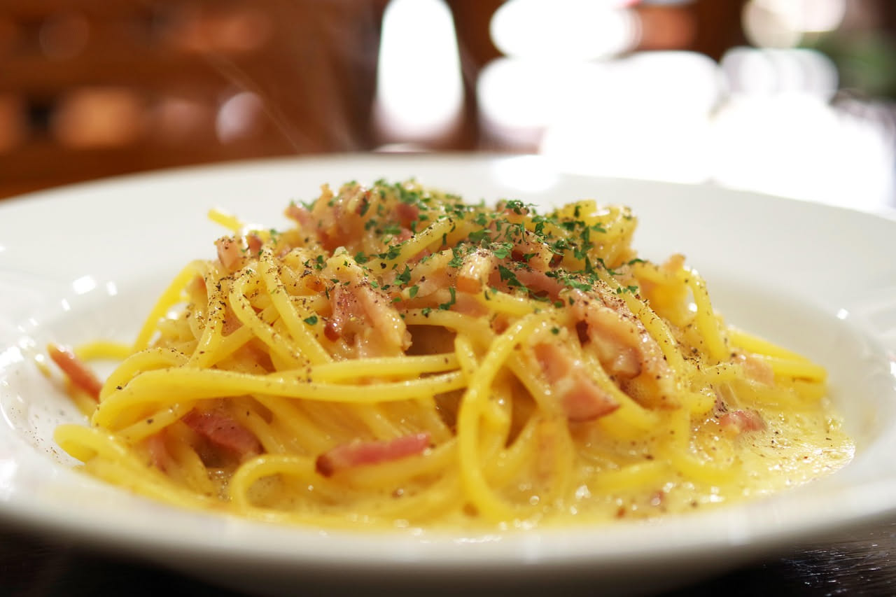 Piatto bianco con spaghetti dritti conditi di olio lucido, con aglio dorato e peperoncino rosso visibile tra i fili di pasta, una spolverata di prezzemolo verde fresco in cima