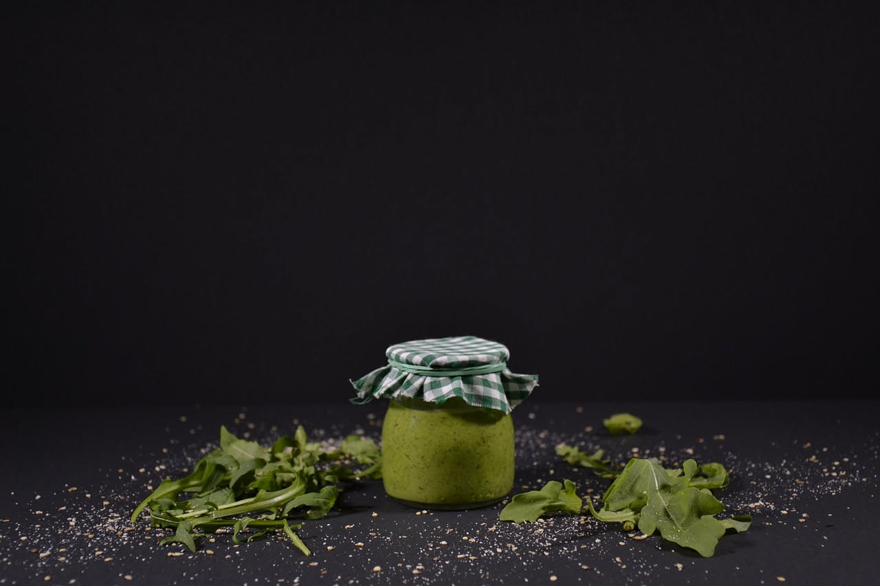 Piatto di spaghetti con rucola selvatica fresca verde, olio lucido, aglio dorato e peperoncino rosso visibile, serviti in piatto bianco fondo con erbe sparse.