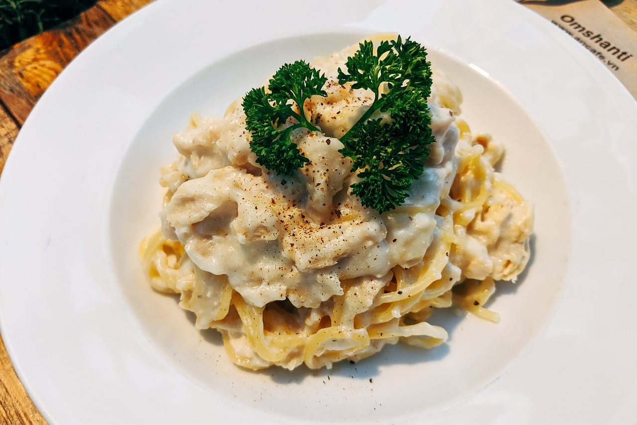 Un piatto bianco con spaghetti bianchi e telline grigie e marrone, bagnat in salsa chiara, guarnito con prezzemolo verde, servito con limone a spicchi sul bordo