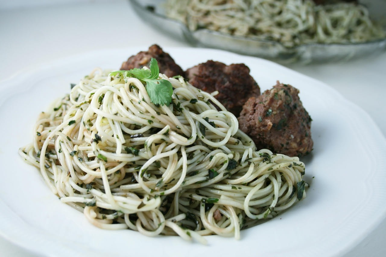 Piatto bianco con spaghetti setosi e cremosi ricoperti da polpa arancione dorata di ricci di mare, cosparsi di prezzemolo fresco verde scuro, con filo di olio d'oliva lucido