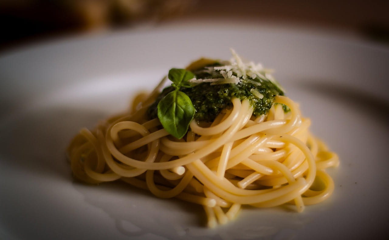 Piatto di spaghetti con le alici appena impiattati: spaghetti dorati e glossati, alici distribuite, olio brillante che riluce, polvere di peperoncino rosso e prezzemolo verde fresco sopra