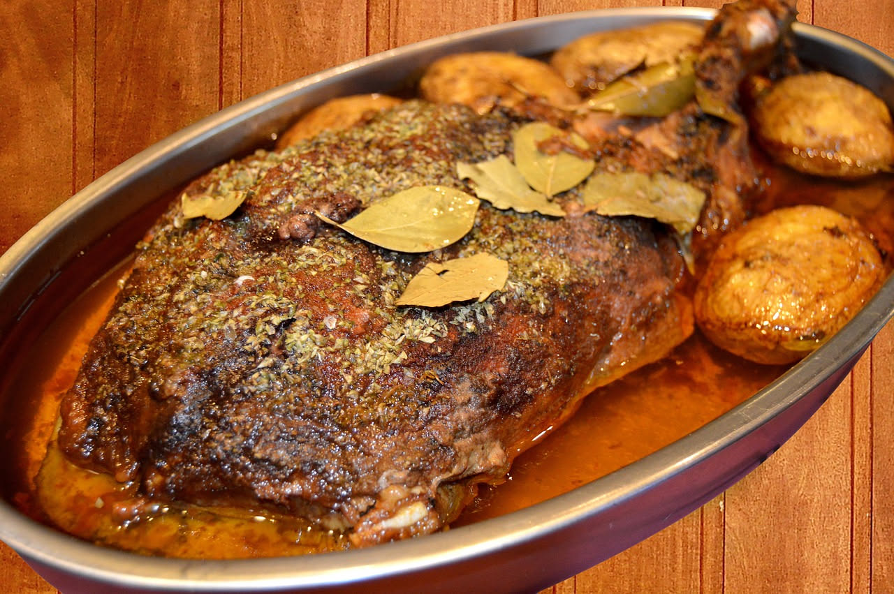 Spalla d'oca intera arrosto, dorata e croccante in superficie, adagiata su un letto di cipolle, carote e sedano caramellati, in una teglia di alluminio con orli rialzati