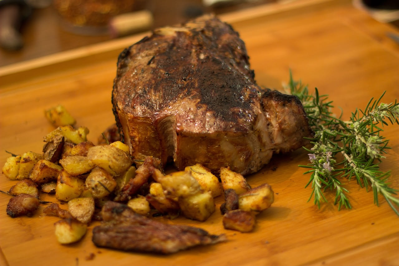 Spalla di San Secondo arrosto cotta al forno, con crosta caramellata, circondata da patate dorate, rosmarino e aglio, in una pirofila di terracotta
