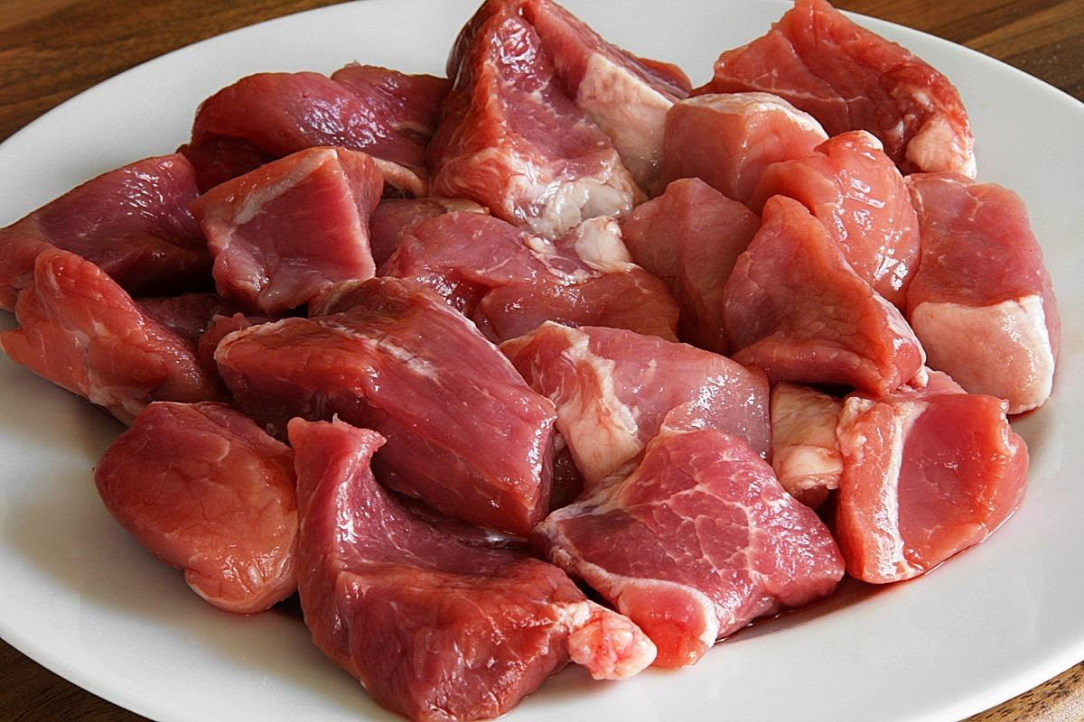 Spezzatino di vitello servito in un piatto fondo bianco, con pezzi di carne rosati teneri, carote arancioni tagliate a rondelle, sedano bianco e prezzemolo fresco. Salsa scura e lucida ricopre la carn
