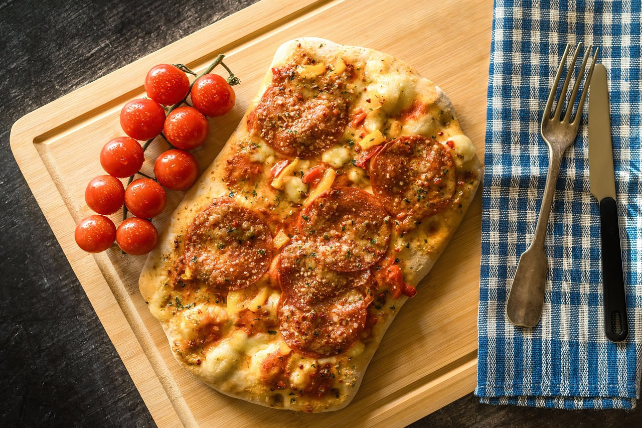 Spianata lucana dorata e croccante in un piatto bianco, con i bordi irregolari e bollicine visibili sulla superficie, condita di strutto lucente e grani di peperoncino rosso, su un fondo di legno scur