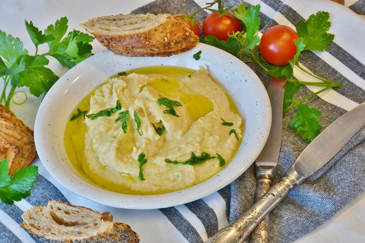 Spuma di ceci beige dorata in una ciotola bianca, decorata con un filo di olio d'oliva e una foglia di prezzemolo fresco