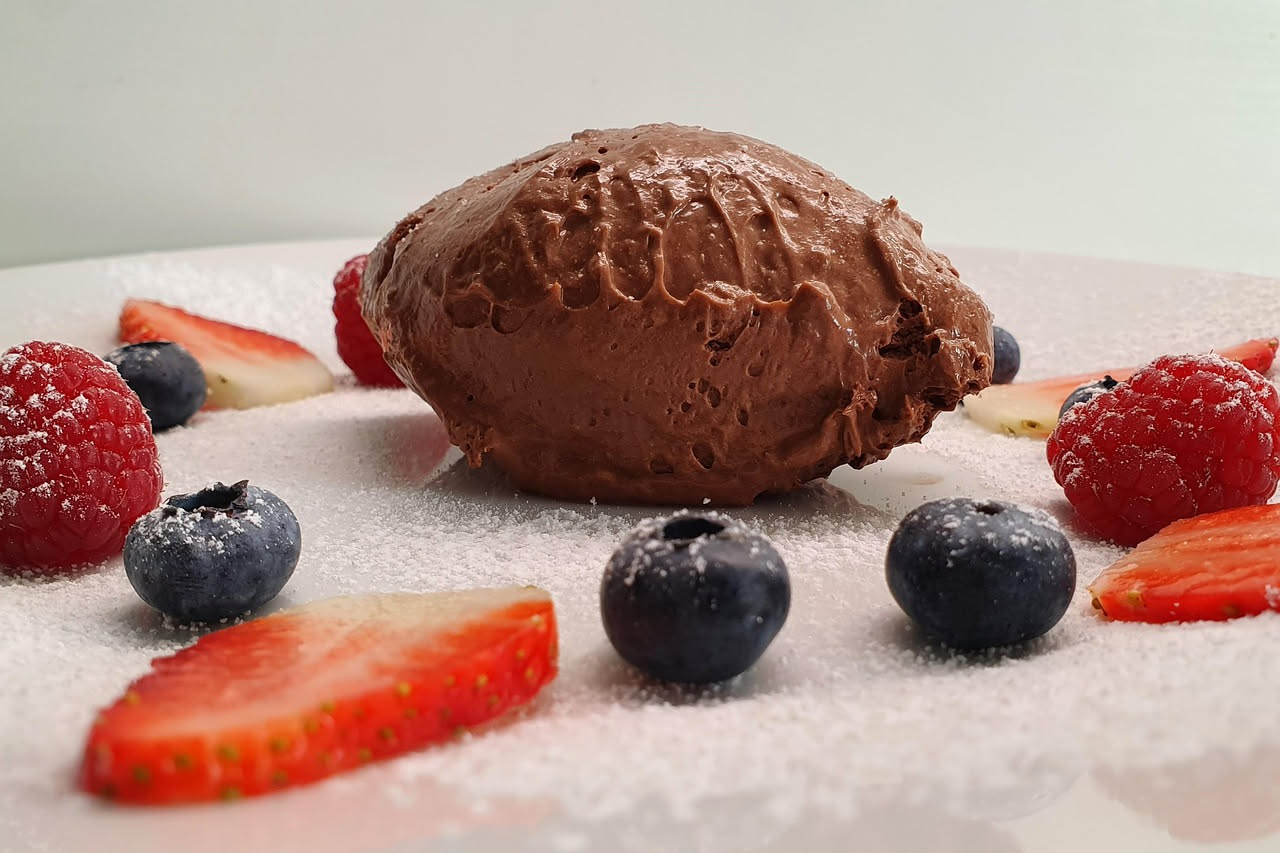 Spuma di fegato marrone chiaro servita in una ciotola bianca, con texture cremosa e levigata, accompagnata da crostini tostati al fianco e un cucchiaio di legno per servire