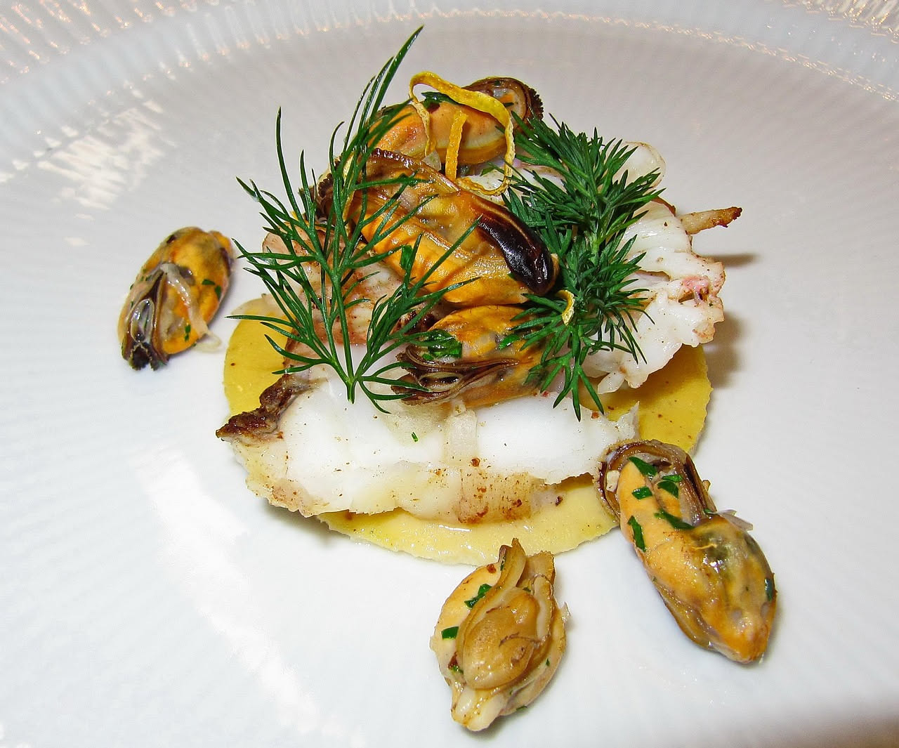 Stoccafisso dissalato in salsa di pomodoro con olive nere e pinoli, servito in un piatto bianco con pane tostato ai lati, salsa rossa che ricopre il pesce, guarnito con prezzemolo fresco